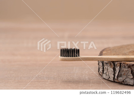 Wooden toothbrush lying on a block of wood on a cream background Wooden toothbrush lying on a block of wood on a cream background 119682496