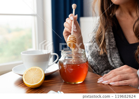 Woman is holding a spoon in a jar of honey 119682624