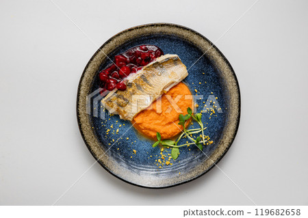 Baked fish fillet with mashed sweet potatoes and berry sauce, served with microgreens garnish 119682658