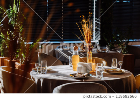 Sunlit restaurant table with elegant glassware, decor, and a warm, cozy ambiance Sunlit restaurant table with elegant glassware, decor, and a warm, cozy ambiance 119682666