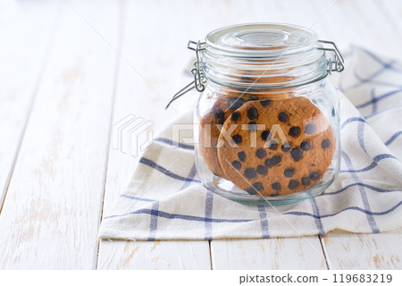 Chocolate chip cookies in a jar, on a light kitchen table, with copy space for text. Glass jar with chocolate chip cookies on a white table. Close-up of a jar full of oatmeal cookies. 119683219