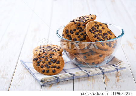 Delicious cookies with chocolate chips in a clear glass bowl with on a light kitchen table, selective focus. Delicious cookies with chocolate chips in a clear glass bowl with on a light kitchen table, selective focus. 119683235