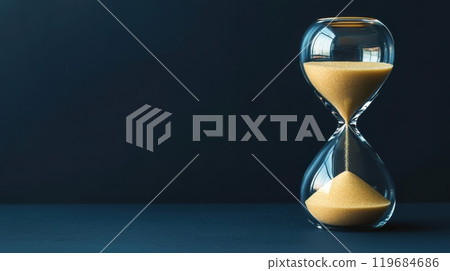 A sand timer is on a table with a blue background 119684686
