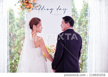 Small wedding - the priest is present, the bride and groom hold their wedding bouquets, hold hands, and share a beautiful moment with family and friends. Small wedding - the priest is present, the bride and groom hold their wedding bouquets, hold hands, and share a beautiful moment with family and friends. 119685856