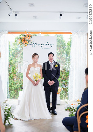 Small wedding - the priest is present, the bride and groom hold their wedding bouquets, hold hands, and share a beautiful moment with family and friends. 119685859