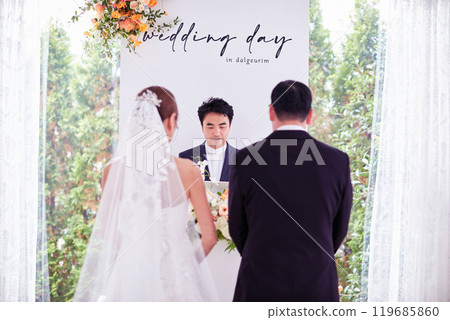 Small wedding - the priest is present, the bride and groom hold their wedding bouquets, hold hands, and share a beautiful moment with family and friends. 119685860