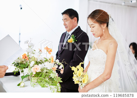 Small wedding - the priest is present, the bride and groom hold their wedding bouquets, hold hands, and share a beautiful moment with family and friends. 119685878