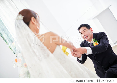 Small wedding - the priest is present, the bride and groom hold their wedding bouquets, hold hands, and share a beautiful moment with family and friends. 119685908