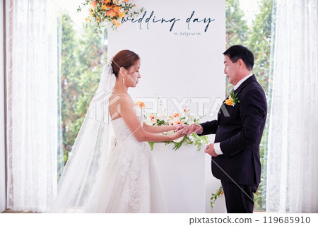 Small wedding - the priest is present, the bride and groom hold their wedding bouquets, hold hands, and share a beautiful moment with family and friends. 119685910