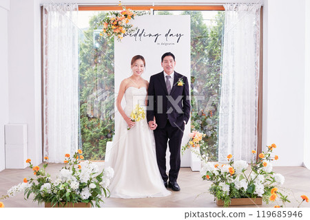 Small wedding - the priest is present, the bride and groom hold their wedding bouquets, hold hands, and share a beautiful moment with family and friends. 119685946