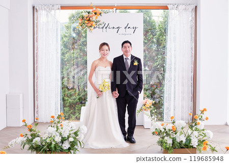 Small wedding - the priest is present, the bride and groom hold their wedding bouquets, hold hands, and share a beautiful moment with family and friends. 119685948