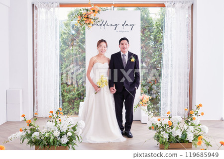 Small wedding - the priest is present, the bride and groom hold their wedding bouquets, hold hands, and share a beautiful moment with family and friends. 119685949