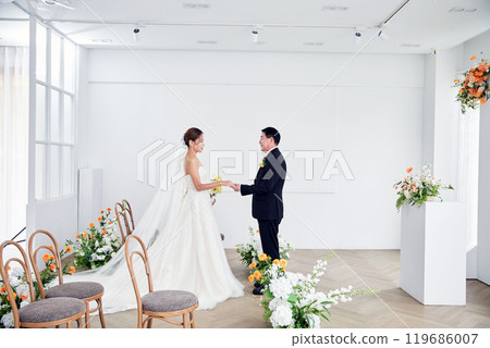 Small wedding - the priest is present, the bride and groom hold their wedding bouquets, hold hands, and share a beautiful moment with family and friends. 119686007