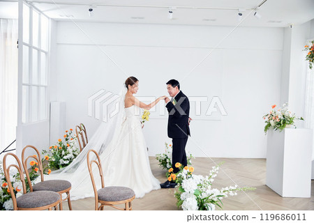 Small wedding - the priest is present, the bride and groom hold their wedding bouquets, hold hands, and share a beautiful moment with family and friends. 119686011