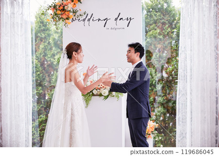 Small wedding - the priest is present, the bride and groom hold their wedding bouquets, hold hands, and share a beautiful moment with family and friends. 119686045