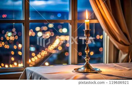 There is a tall candlestick with a burning candle on the table 119686921