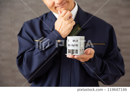 A middle-aged male businessman in work clothes worried about an architectural model of a building 119687186
