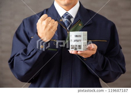 A middle-aged male businessman in work clothes making a fist pump while holding an architectural model of a building A middle-aged male businessman in work clothes making a fist pump while holding an architectural model of a building 119687187