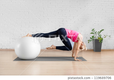 Fit adult woman in pink tank top pulling the knee up to the chin from the plank position using fitness ball in studio indoor. Fit adult woman in pink tank top pulling the knee up to the chin from the plank position using fitness ball in studio indoor. 119689706