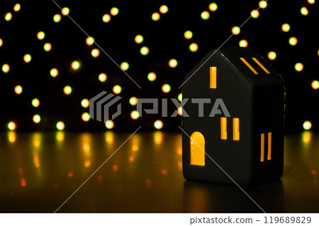 Christmas clay lantern house on dark bokeh light garland background. New year and Christmas preparation. Handmade eco-friendly decor. Sustainable Christmas decoration Christmas clay lantern house on dark bokeh light garland background. New year and Christmas preparation. Handmade eco-friendly decor. Sustainable Christmas decoration 119689829
