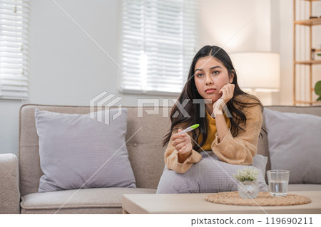 Woman Checking Pregnancy Test Kit at Home, Sitting on Sofa with Thoughtful Expression, Awaiting Results 119690211