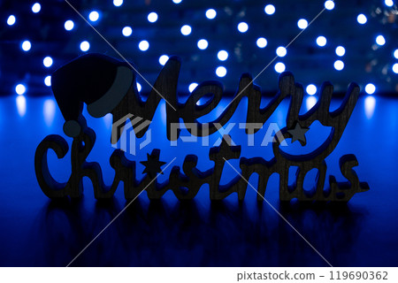 Merry Christmas wooden message on dark bokeh light garland background. New year and Christmas preparation. Handmade eco-friendly decor. Sustainable Merry Christmas wooden message on dark bokeh light garland background. New year and Christmas preparation. Handmade eco-friendly decor. Sustainable 119690362