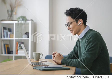 A man in his 40s wearing earphones and facing a laptop 119691191