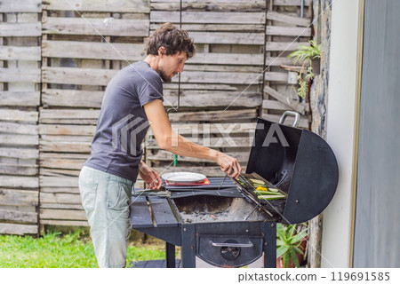 Man cooking dinner on a barbecue in his backyard. Outdoor cooking, home lifestyle, and family time concept 119691585