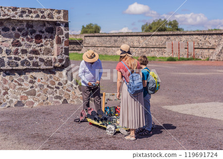 Mother and son tourists buying Mexican souvenirs from a street vendor at the foot of the Teotihuacan pyramid. Cultural experience, travel, and local craftsmanship concept 119691724