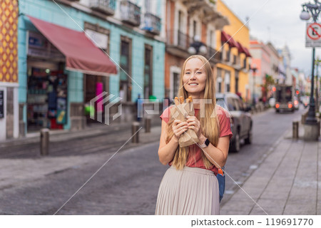 Female tourist eating churros on a colonial street in Puebla, Mexico. Cultural experience, local cuisine, and street food exploration concept Female tourist eating churros on a colonial street in Puebla, Mexico. Cultural experience, local cuisine, and street food exploration concept 119691770