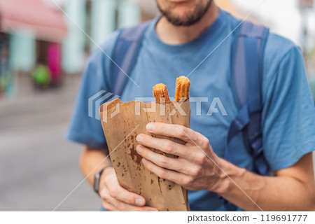 Male tourist eating churros on a colonial street in Puebla, Mexico. Cultural experience, local cuisine, and street food exploration concept Male tourist eating churros on a colonial street in Puebla, Mexico. Cultural experience, local cuisine, and street food exploration concept 119691777
