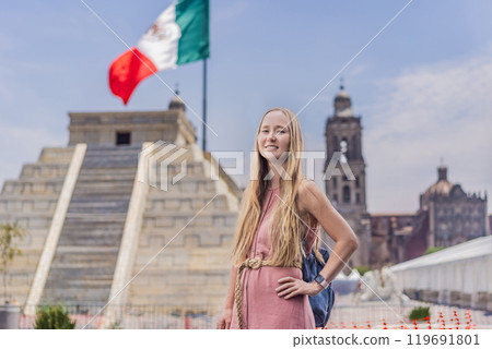 Woman tourist exploring the historic Zocalo square in Mexico City, standing in front of a replica Aztec pyramid with the Mexican flag waving in the background. The Metropolitan Cathedral can be seen 119691801