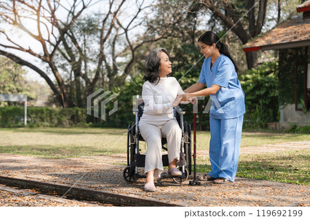 Elderly Woman in Wheelchair Assisted by Caregiver Outdoor During Rehabilitation Therapy Session Elderly Woman in Wheelchair Assisted by Caregiver Outdoor During Rehabilitation Therapy Session 119692199