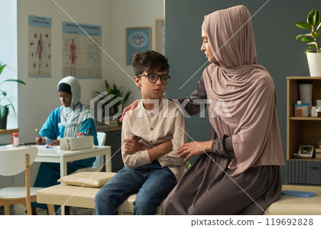 Muslim Woman Consoling Child in Doctor's Office Setting 119692828