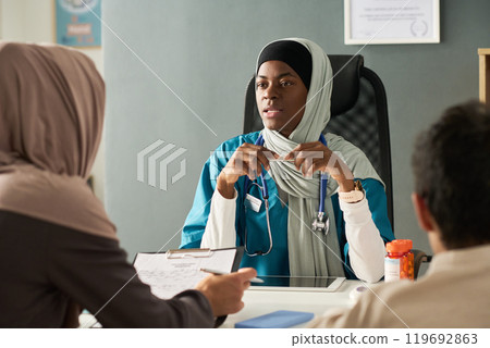Muslim Doctor Listening to Patient in Medical Office Setting 119692863