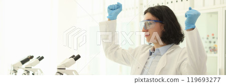 Joyful male scientist in protective goggles raises hands 119693277