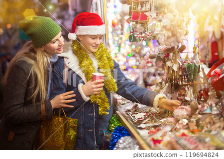 Smiling teen girl with mother choosing Christmas decorations at street fair Smiling teen girl with mother choosing Christmas decorations at street fair 119694824