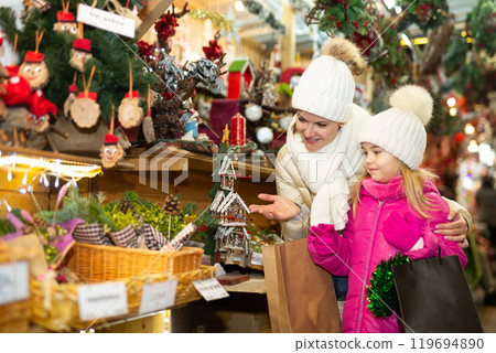 Joyous mother with little daughter buying decorations for Xmas at an open air market Joyous mother with little daughter buying decorations for Xmas at an open air market 119694890