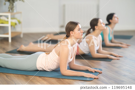Young girl teaches yoga lesson, shows students technique of performing Urdhva Mukha Shvanasana asana Young girl teaches yoga lesson, shows students technique of performing Urdhva Mukha Shvanasana asana 119695148