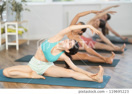 Girl teaches yoga lesson, shows students technique of performing Parivritta Janu Shirshasana asana 119695223