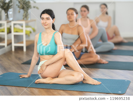 Women maintaining mental and physical health attending group yoga class at modern studio, practicing twisting pose 119695238