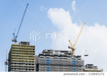 Low-angle view of cranes and steel structures of building construction with a blue sky background. Low-angle view of cranes and steel structures of building construction with a blue sky background. 119695272