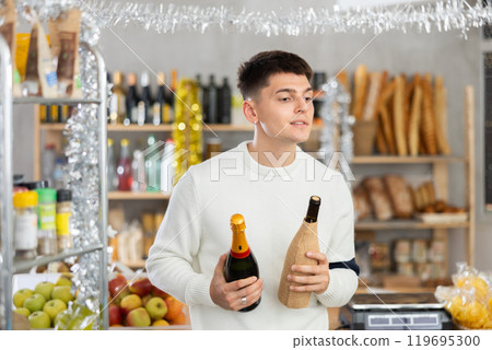 Young guy is choosing wine in grocery store during New Year Young guy is choosing wine in grocery store during New Year 119695300