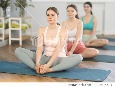Young girl teaches yoga lesson, shows students technique of performing butterfly pose asana 119695304