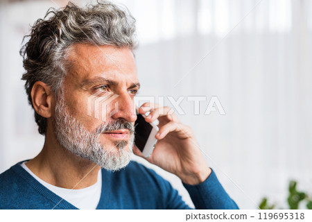 Portrait of handsome man making phone call, looking out of window and smiling. 119695318