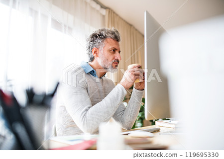Homeoffice for handsome man. Man drinking coffee in the morning, working on computer from home. Telecommuting. Homeoffice for handsome man. Man drinking coffee in the morning, working on computer from home. Telecommuting. 119695330