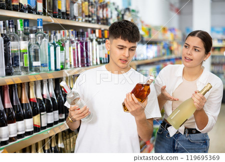 Man and woman choose high-quality alcoholic drink in supermarket 119695369