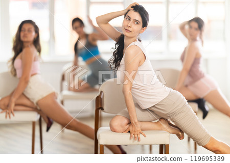 Girl sitting on knees on chair performs lap dance. Female students repeat erotic movements 119695389