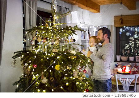 Father showing christmas tree to little son in Christmas home. Cute baby boy is amazed by christmas decorations. 119695400