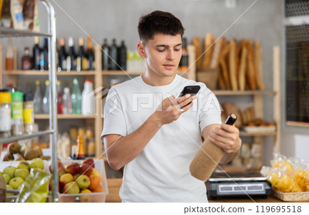 Young guy purchaser scanning with smartphone QR code label of bottle of wine in shop Young guy purchaser scanning with smartphone QR code label of bottle of wine in shop 119695518